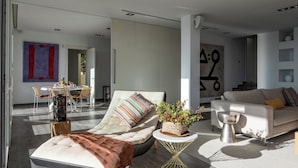 A modern living room with a sofa, a chaise lounge, a dining area, and a staircase.