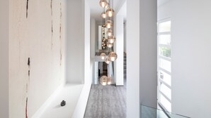 A modern interior with a minimalist design, featuring a long hallway with a unique wall art installation and a series of spherical pendant lights.
