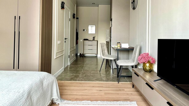 A modern bedroom with a bed, a desk with a chair, a TV, and a small table with a vase.