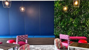 Un interior moderno con pared azul, pared verde con plantas, sillas rojas y con estampado, y lámparas colgantes.