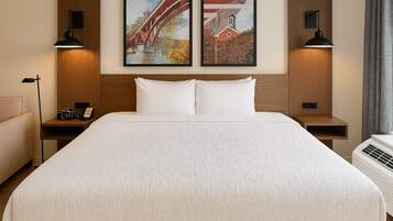 A hotel room with a large bed, two wall-mounted lamps, a wooden headboard, and two framed pictures.