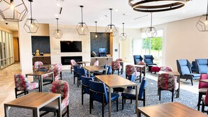 Un vestíbulo moderno de hotel con lámparas colgantes hexagonales, un televisor de pantalla plana, una chimenea y una mezcla de sillones tapizados en azul y tartán.