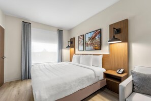 A hotel room with a large bed, a bedside table with a phone, and two wall-mounted lamps. - Hawthorn Extended Stay by Wyndham Mebane (Mebane)