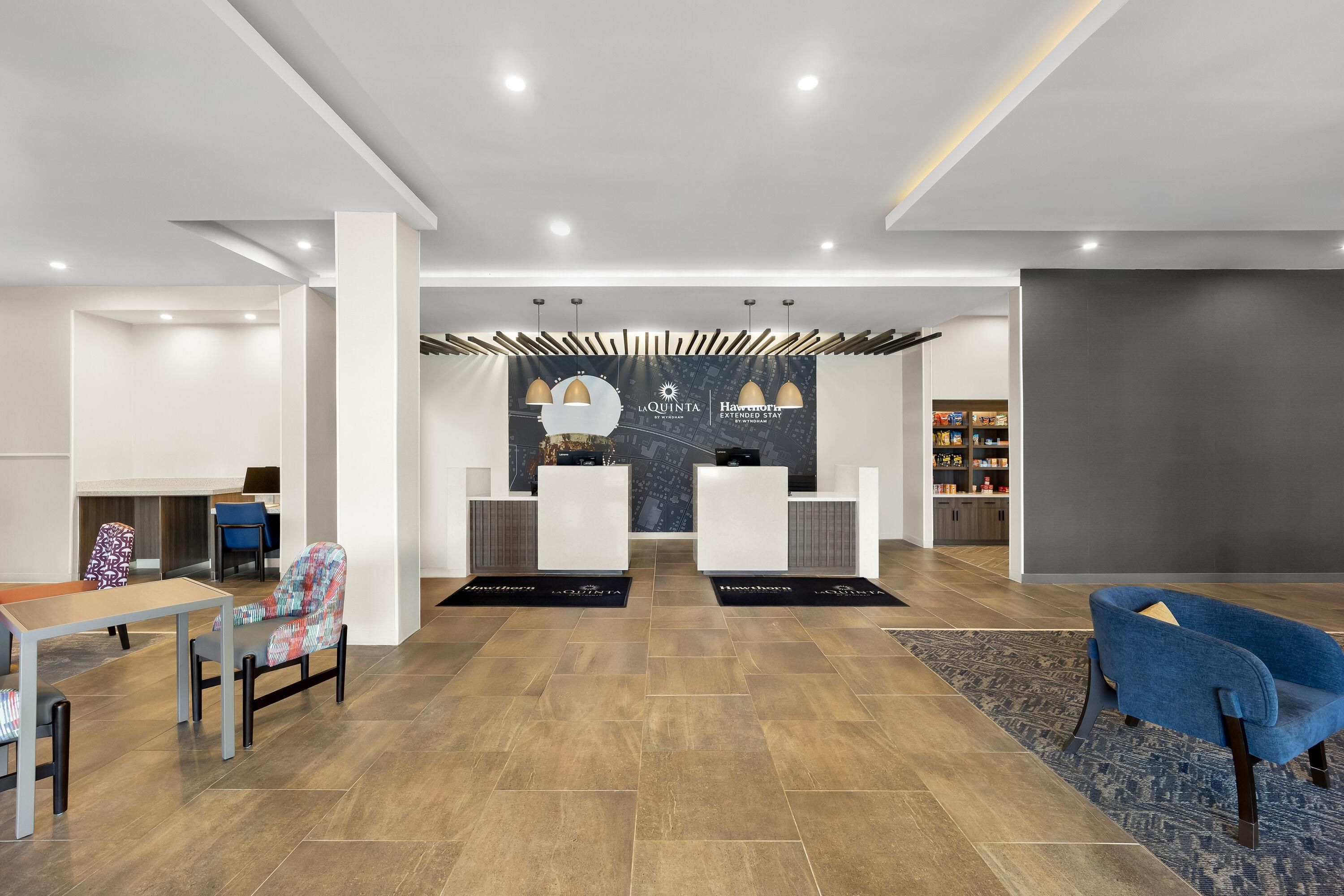 A modern reception area with a reception desk, two chairs, a coffee machine, and a seating area with a table and chairs.