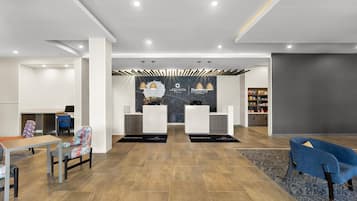 A modern reception area with a reception desk, two chairs, a coffee machine, and a seating area with a table and chairs.