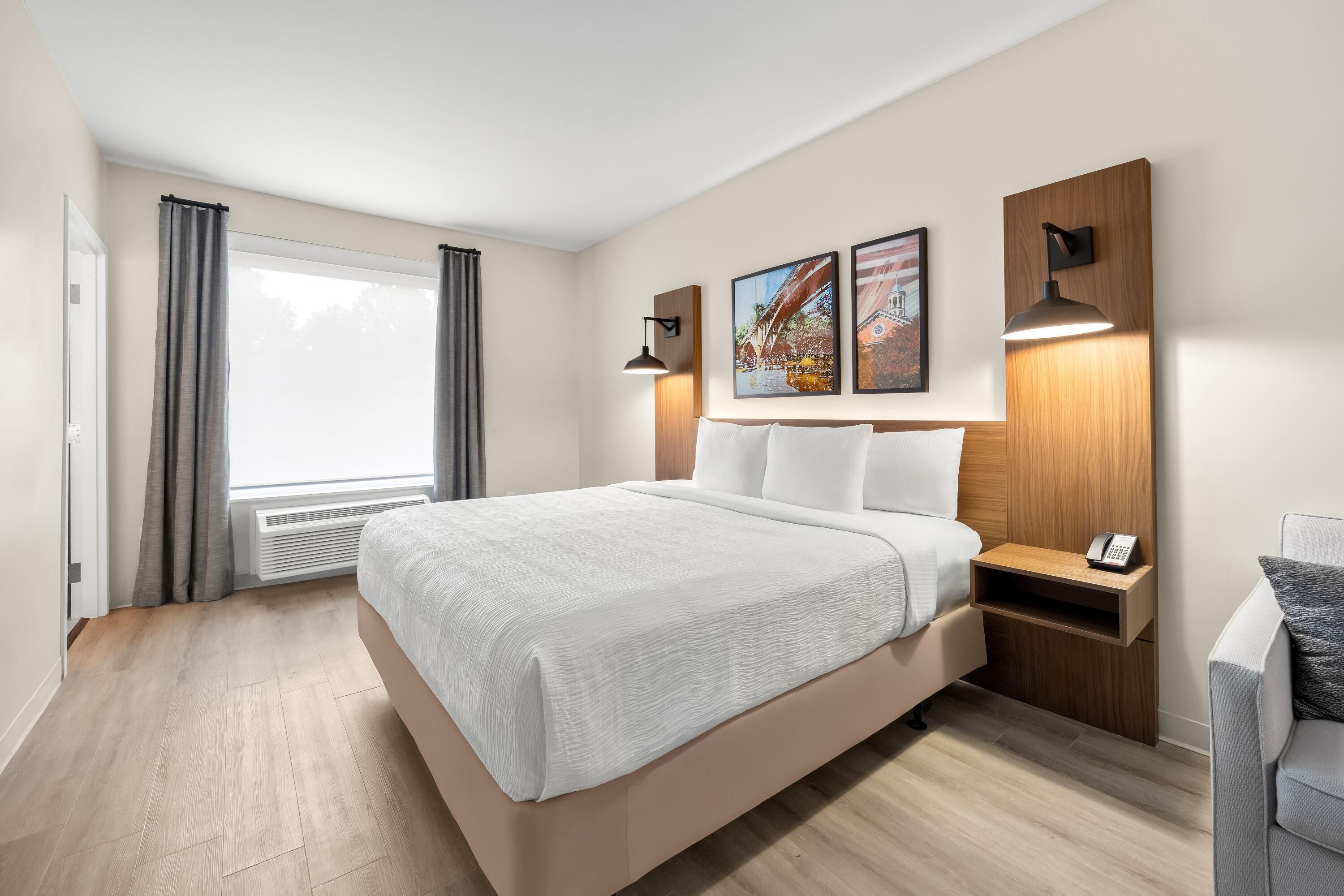 Una habitación de hotel moderna con una cama grande, una mesita de noche con teléfono y una ventana con cortinas.
