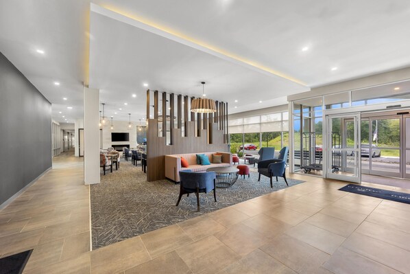 A modern hotel lobby with a seating area, a fireplace, and a large window offering a view of the outdoors. - Hawthorn Extended Stay by Wyndham Mebane (Mebane)