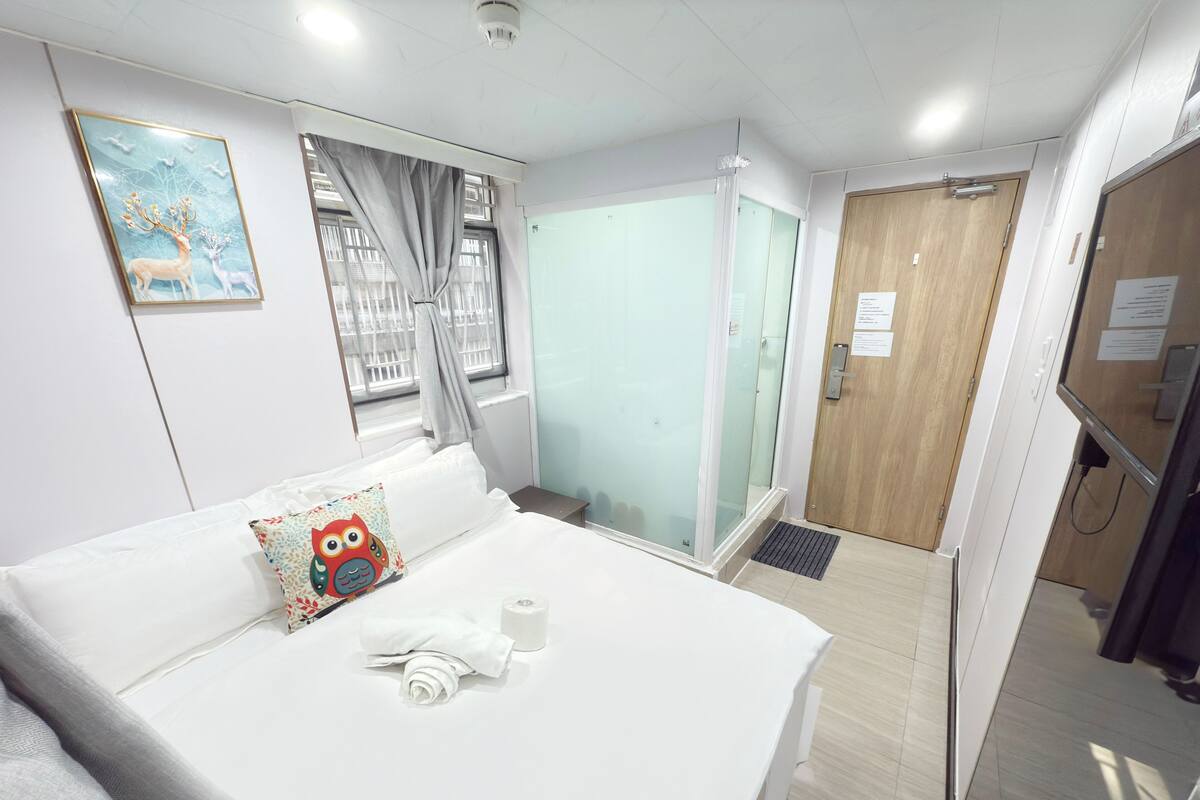 A hotel room with a bed, a window with curtains, a door, and a wall-mounted picture.