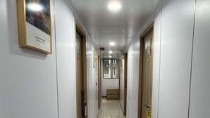 A long, narrow hallway with doors on both sides, a bench in the center, and a framed picture on the left wall. - Fortune Inn (Kowloon)