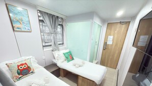 A small, clean room with two single beds, a window with curtains, a wooden door, and a wall-mounted painting of deer. - Fortune Inn (Kowloon)