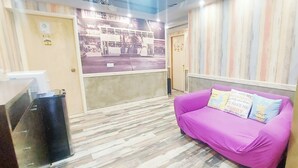 A room with a purple sofa, a small trash bin, a refrigerator, and a wall with a poster. - Fortune Inn (Kowloon)