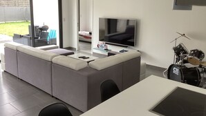 En moderne stue med en modulsofa, et fladskærms-tv, et trommesæt og et spiseområde.