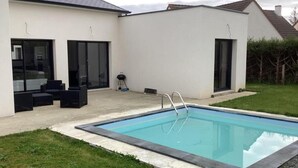 Et moderne hus med swimmingpool, store skydedøre og udendørs møbler.