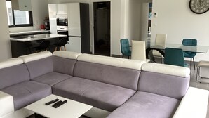 En moderne stue med en grå hjørnesofa, et hvidt sofabord og et spiseområde med et glasbord samt teal stole.