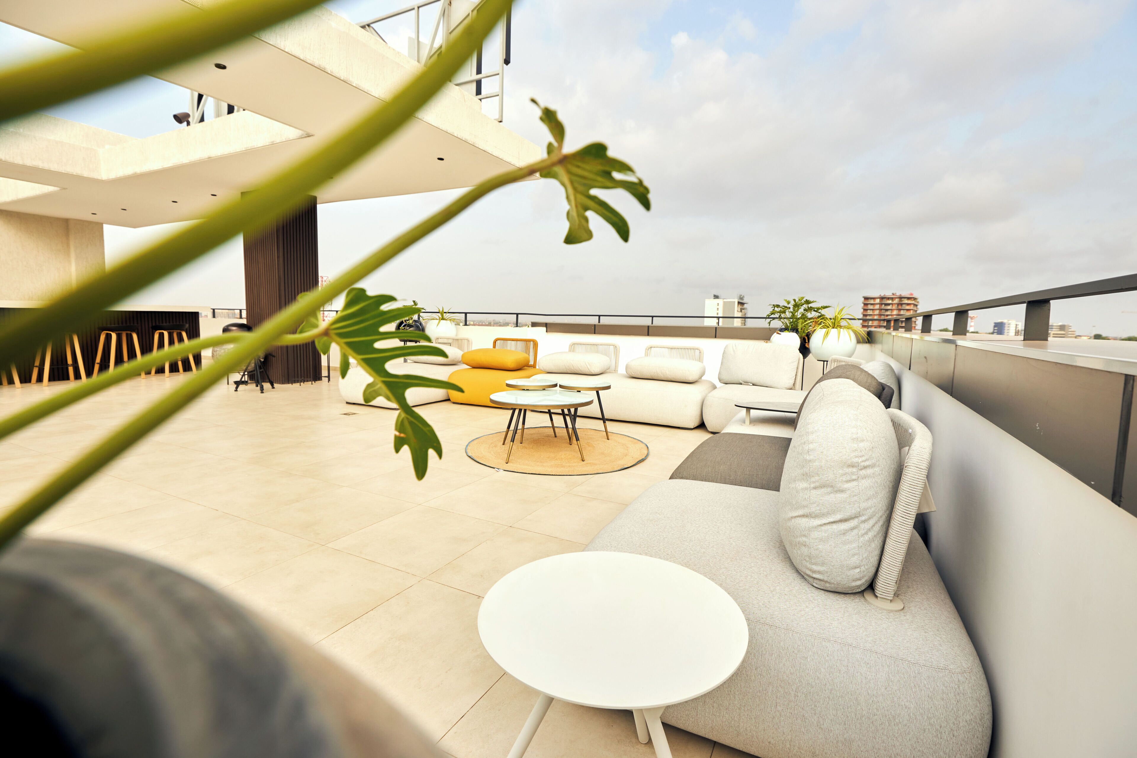 A modern rooftop lounge with a sofa, round tables, and potted plants.