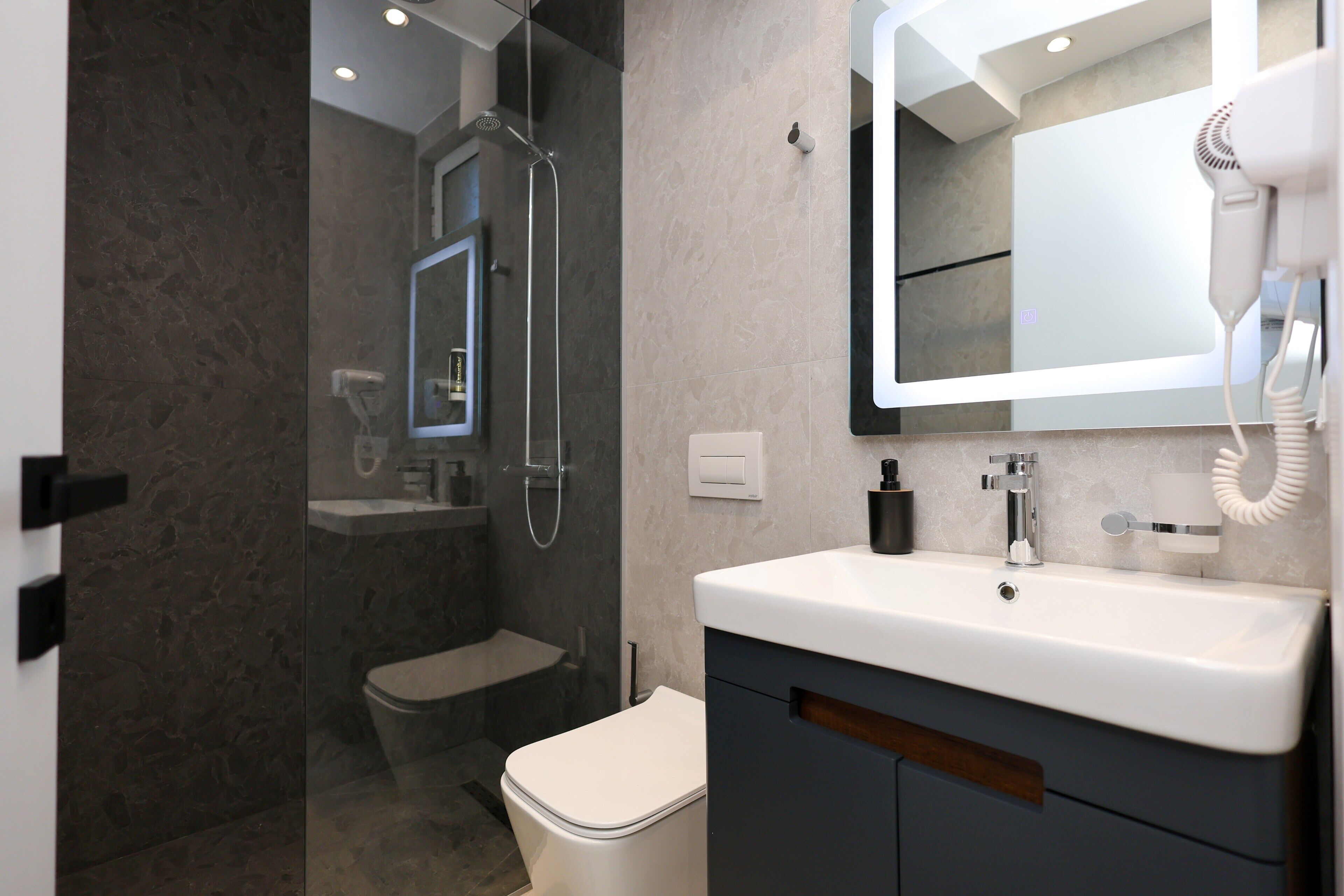 A modern bathroom with a glass-enclosed shower, a toilet, a sink with a mirror, and a hairdryer on the countertop.