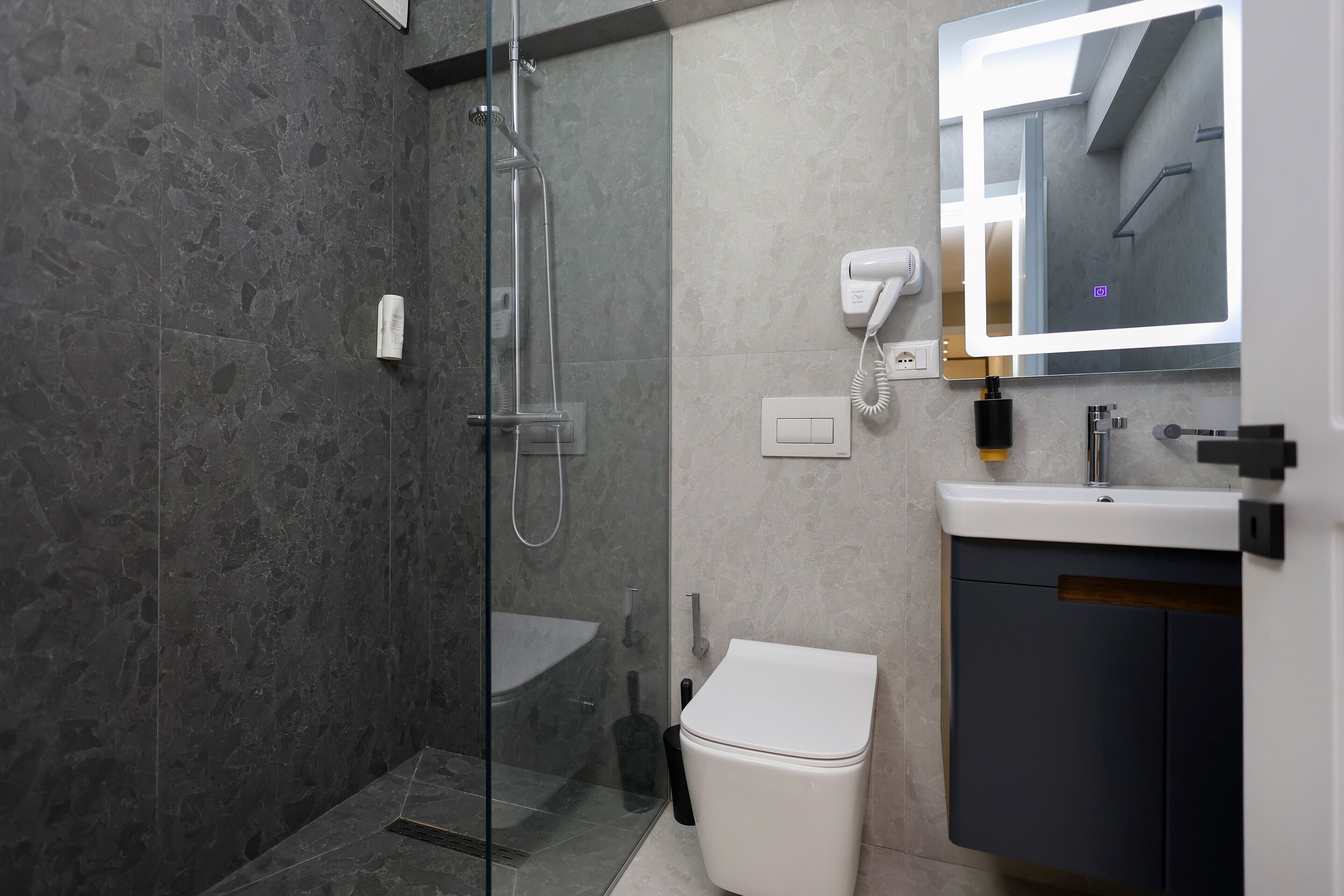 A modern bathroom with a glass-enclosed shower, a white toilet, a sink with a mirror, and a hairdryer.