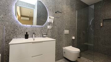 Un baño moderno con encimera de granito, un lavabo blanco, un espejo redondo, inodoro y ducha con mampara de vidrio.