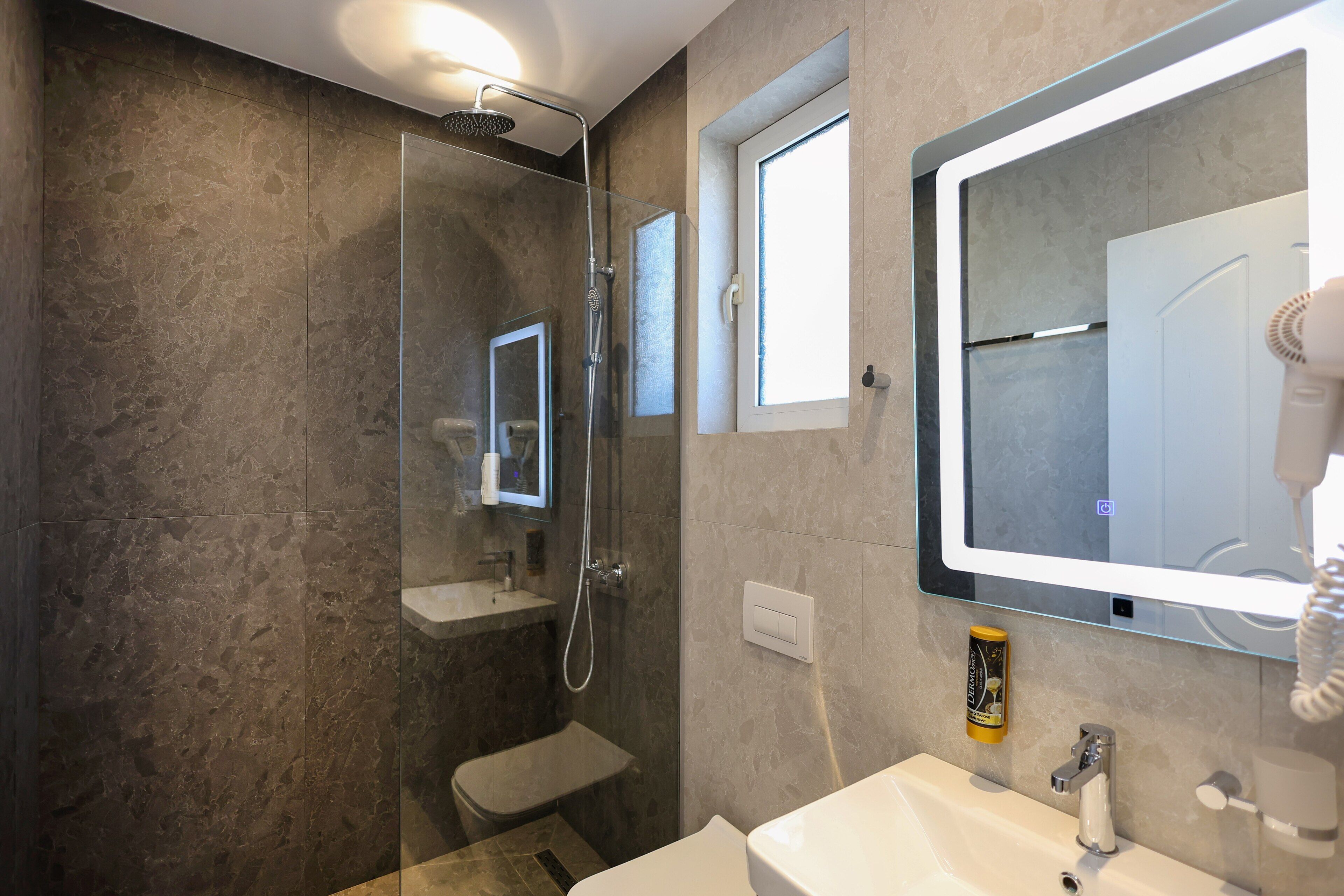 A modern bathroom with a glass-enclosed shower, a large mirror, and a white sink.