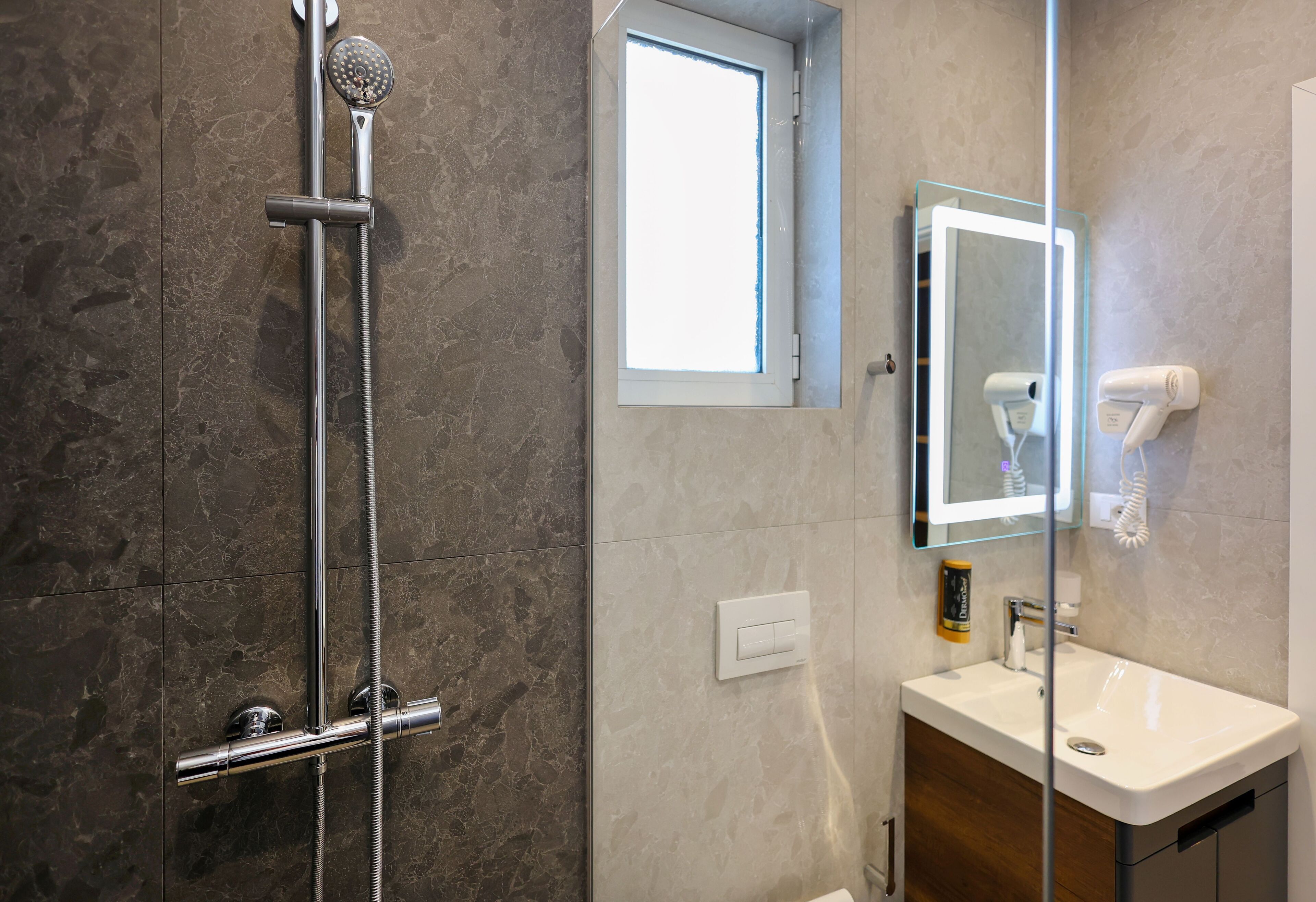 A modern bathroom with a glass shower enclosure, a vanity with a mirror, and a hairdryer mounted on the wall.