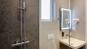 A modern bathroom with a glass shower enclosure, a vanity with a mirror, and a hairdryer mounted on the wall.
