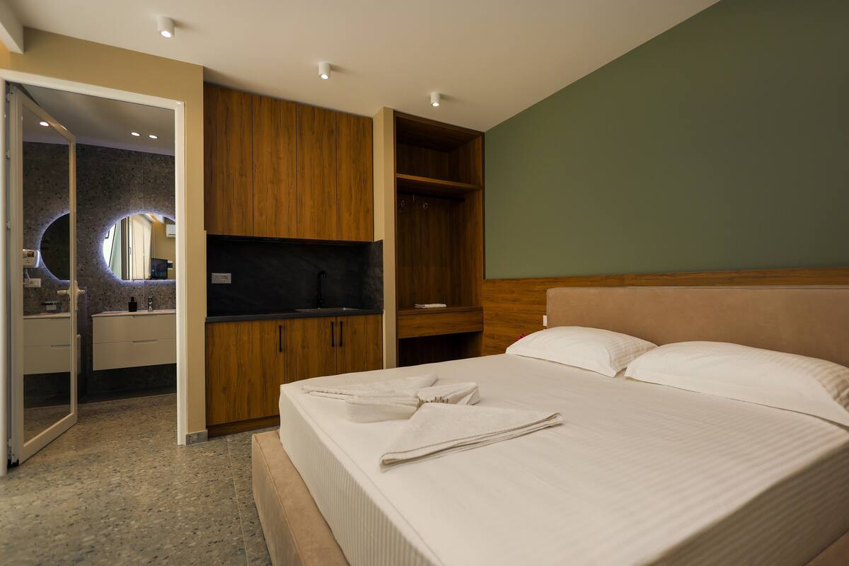 A hotel room with a bed, a wooden wardrobe, a built-in vanity, and a mirror.