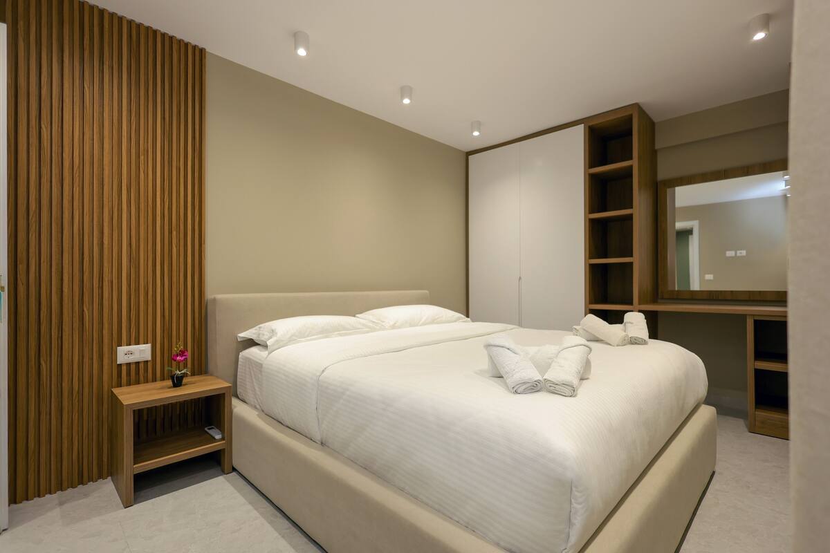 A modern bedroom with a large bed, a bedside table with a vase, and a built-in wardrobe.