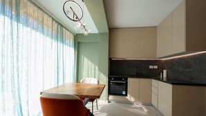 A modern kitchen with a built-in oven, a dining area with a wooden table and orange chairs, and a large window with sheer curtains. - Apartments Luxury Mimani 2 (Velabisht)