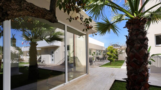 A modern house with a glass door leading to a patio, surrounded by palm trees and a well-maintained lawn. - Apartments Luxury Mimani 2 (Velabisht)