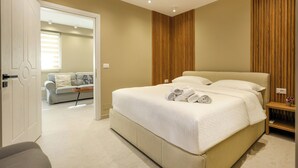 A modern bedroom with a large bed, a wooden panel wall, and a view into another room with a sofa. - Apartments Luxury Mimani 2 (Velabisht)