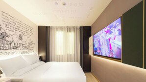 Moderni hotellihuone, jossa on suuri sänky, taulutelevisio ja seinä, jossa on tekstiä ja piirustuksia.