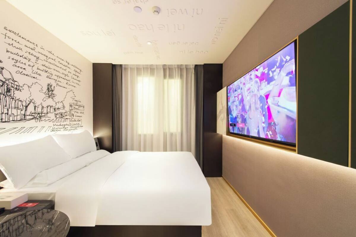 A modern hotel room with a large bed, a flat-screen TV, and a wall with text and drawings.