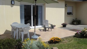 Une terrasse avec une table et des chaises, un fauteuil, une plante en pot et un grand parasol.