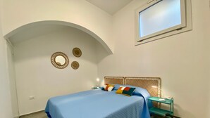 A bedroom with a bed, a bedside table, a lamp, a chair, and a window. - Casa La Mamà, 150 meters from the sea (ALCAMO)