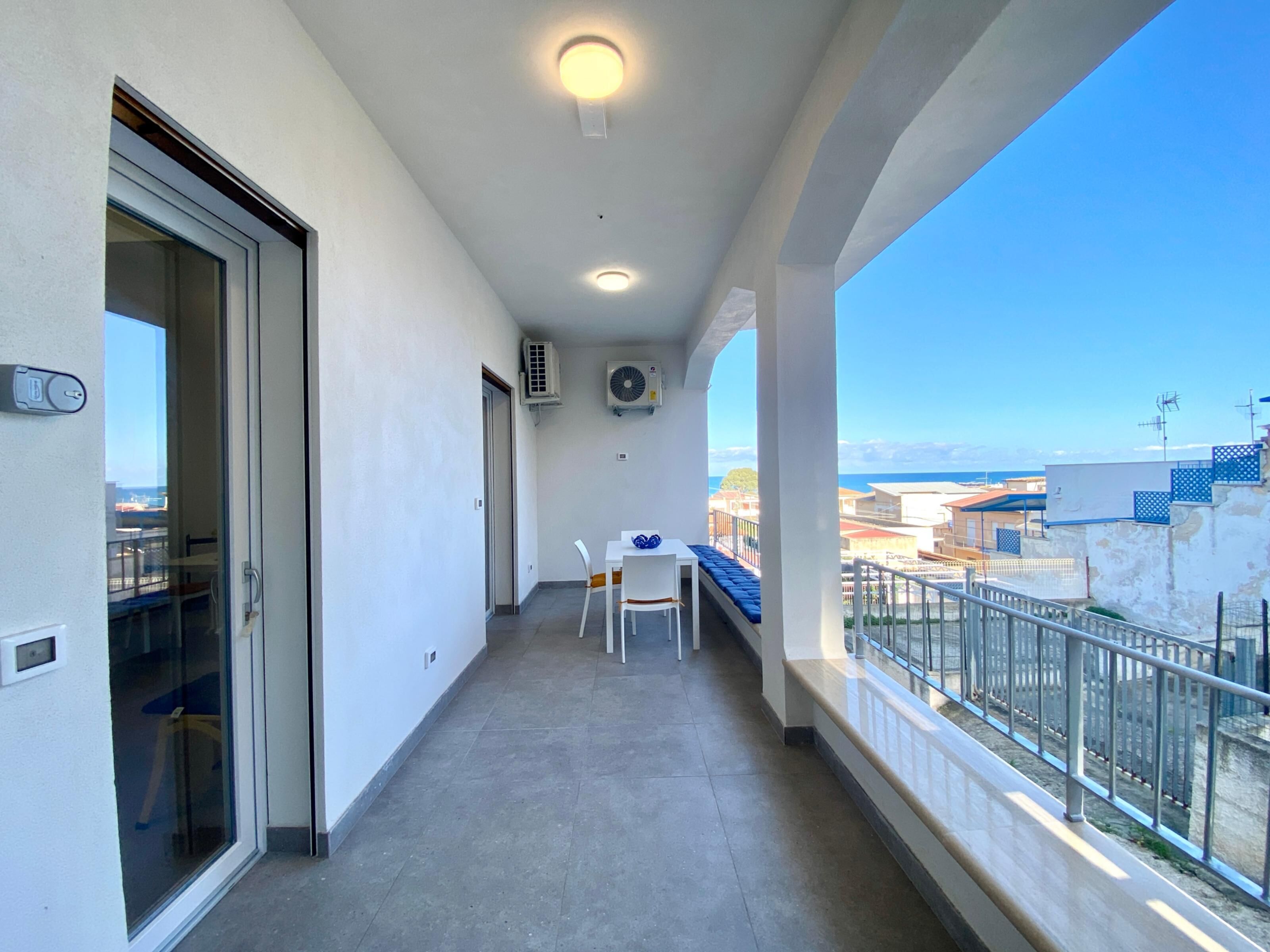 Ein schmaler Balkon mit Meerblick, ein Tisch mit Stühlen und eine Klimaanlage.