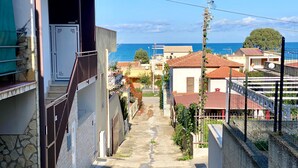 A narrow street leading to a coastal area with buildings, a stone wall, and a view of the sea. - Casa La Mamà, 150 meters from the sea (ALCAMO)