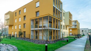 A modern multi-story building with a yellow facade, large windows, and a central courtyard with a tree. - Le Blue Dock - Port de Vannes (Vannes)