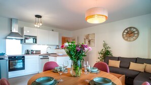 A modern kitchen with white cabinets, a built-in oven, and a dining area with a wooden table set for four. - Le Blue Dock - Port de Vannes (Vannes)