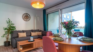 A modern living room with a sofa, coffee table, dining table, chairs, and a large window with a view. - Le Blue Dock - Port de Vannes (Vannes)