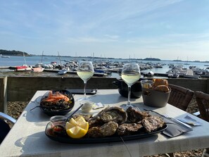 Ein Tisch mit Meeresfrüchten, zwei Gläsern Weißwein und Brot mit Blick auf das Wasser.