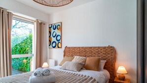 A neatly made bed with a striped blanket, a headboard with a woven design, and a wall-mounted abstract painting. - Les Voiles Arradonnaises - Proche sentier côtier (Arradon)