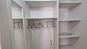 A walk-in closet with multiple shelves, a broom, and a mirror. - Ivy Place Studio Apartment (Cape Town)