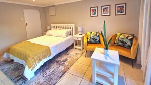 A bedroom with a bed, bedside table, nightstand, and a sofa with a plant. - Ivy Place Studio Apartment (Cape Town)