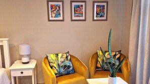 A room with two yellow armchairs, a white side table, a white table, and three framed artworks on the wall. - Ivy Place Studio Apartment (Cape Town)