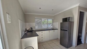 A compact kitchen with white cabinets, a stainless steel refrigerator, and a window with blinds. - Ivy Place Studio Apartment (Cape Town)
