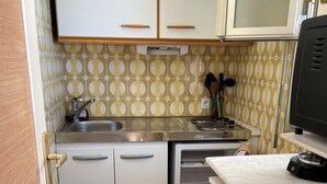 A compact kitchen with white cabinets, a stainless steel sink, and a microwave.