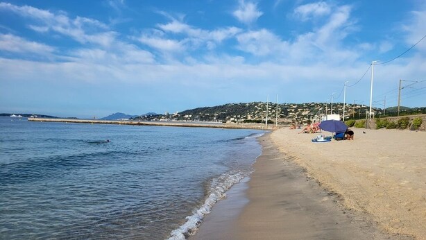 A beach with clear water, a sandy shore, and a distant town.