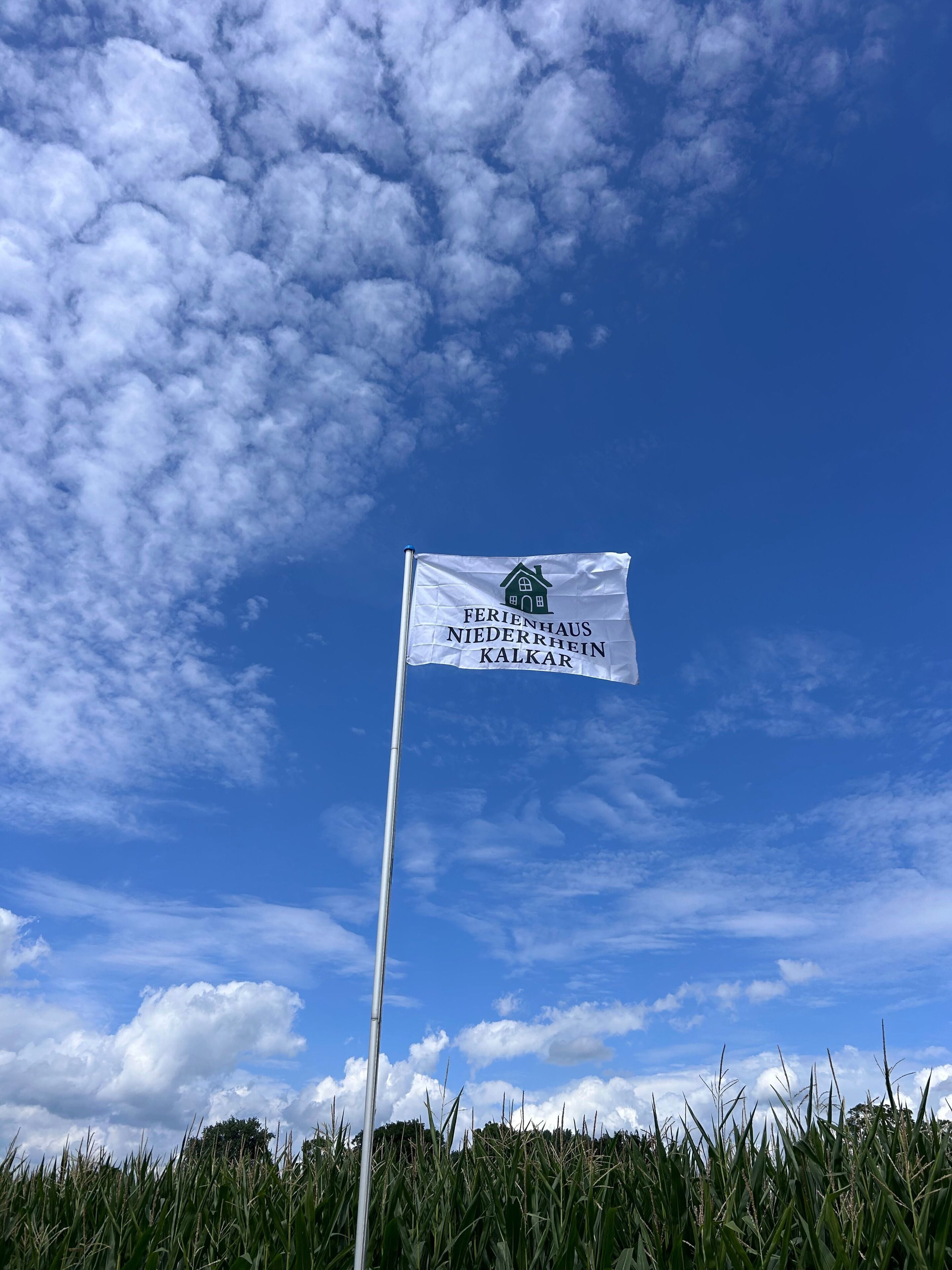 En flagga med ett hus och text på, mot en bakgrund av blå himmel och moln.