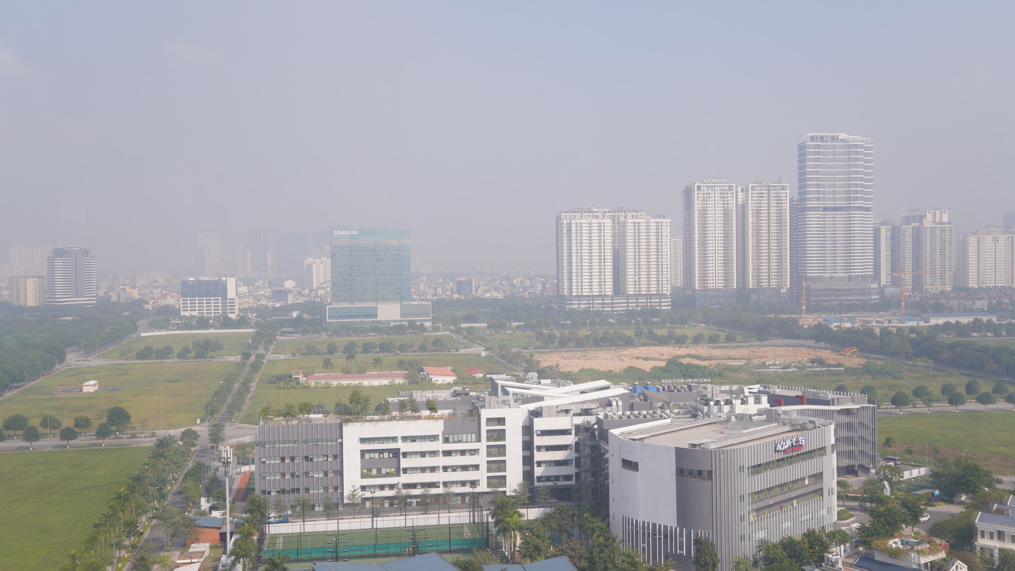 A high-rise building with a modern design, surrounded by other high-rise buildings and a green park area.