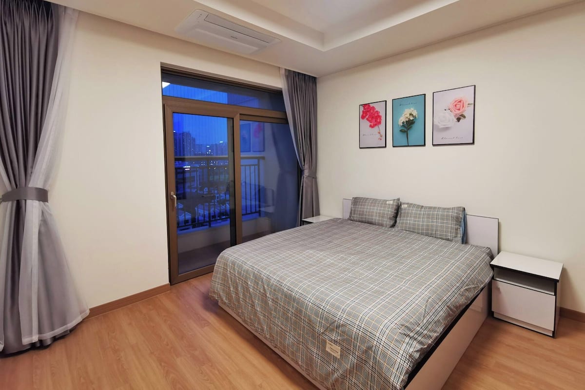 A bedroom with a large bed, a nightstand, a window with curtains, and three framed pictures on the wall.